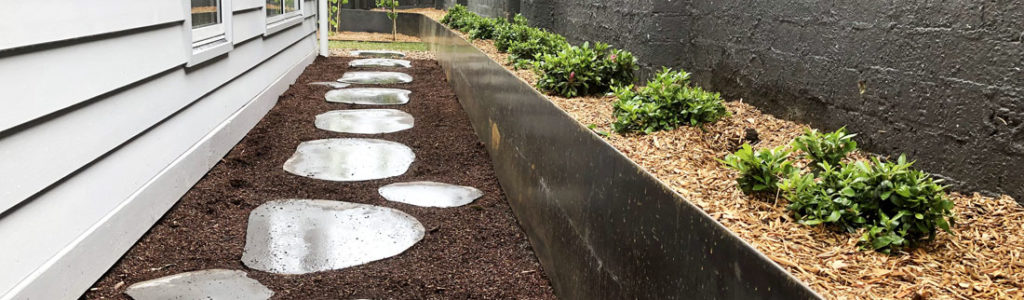 Raised garden bed created with Straightcurve steel edging along a narrow pathway with stepping stones, showcasing a clean and organized backyard garden design.