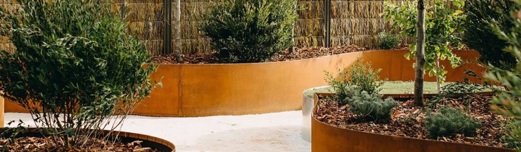 Curved steel garden edging creating distinct, raised planters with greenery, enhancing a modern landscape design.