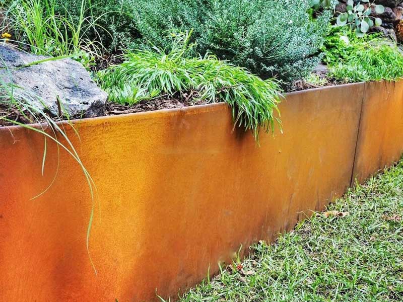 Corten steel garden edging with a developed orange-brown patina in a landscaped garden border