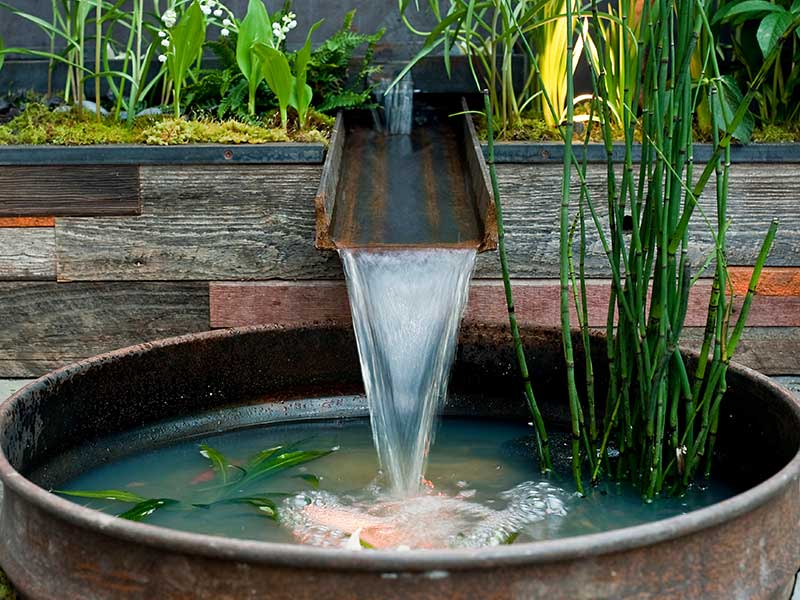 Weathering steel water feature in a garden, a challenging application due to constant moisture exposure disrupting patina formation